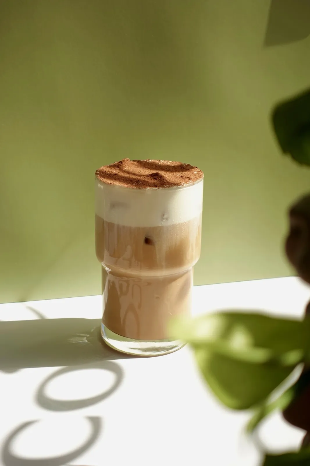 Tiramisu latte dusted with cocoa, shot against a sage green wall